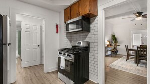A kitchen with a stove, microwave, and wooden cabinets. There is a dining area with a table and chairs. - The Lucile - Spacious 4BR Extended-Stay Home | Fast Wi-Fi & Parking (Wichita Falls)