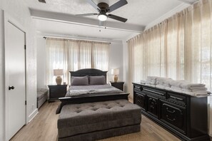 A bedroom with a bed, bedside tables, a dresser, a ceiling fan, and curtains. - The Lucile - Spacious 4BR Extended-Stay Home | Fast Wi-Fi & Parking (Wichita Falls)