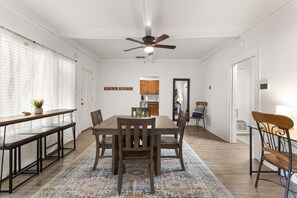 A dining area with a wooden table, chairs, a patterned rug, and a ceiling fan. - The Lucile - Spacious 4BR Extended-Stay Home | Fast Wi-Fi & Parking (Wichita Falls)