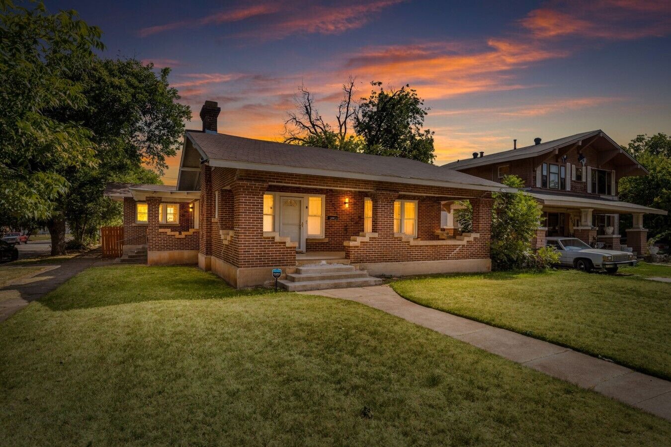 A two-story brick house with a front porch, a driveway, and a car parked in the driveway.