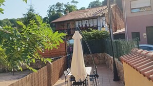 An outdoor patio area with a table and chairs, a hanging umbrella, and a view of a building with a tiled roof. - Superb 3-bedroom townhome in charming Liérganes awaits you (Liérganes)