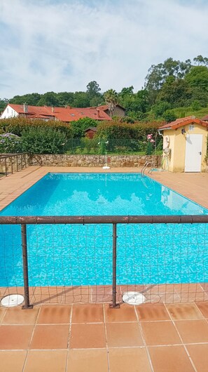 Ein rechteckiger Swimmingpool mit Fliesenveranda, umgeben von einer Steinmauer und einem Metallzaun.
