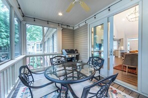 A covered patio with a glass table and chairs, a grill, and a view of the neighborhood.