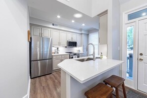 A modern kitchen with stainless steel appliances, white cabinetry, and a central island with stools. - Lakefront Condo • Marina Access • 3BR Screened Porch (Greensboro)