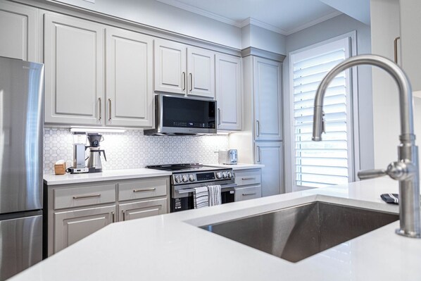 A modern kitchen with white cabinets, stainless steel appliances, a microwave, stove, oven, and a sink.
