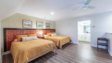A hotel room with two beds, a ceiling fan, a small table, and a view of the kitchen.