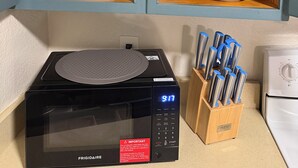 Une cuisine équipée d’un four à micro-ondes, d’un bloc à couteaux et d’un meuble contenant de la vaisselle et des verres.