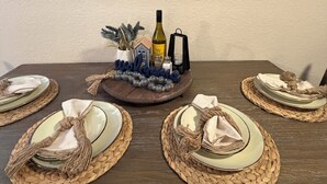 Une table à manger dressée avec des sets de table en fibres tressées, des assiettes et une bouteille de vin.