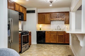 A compact kitchen with wooden cabinets, a stainless steel refrigerator, a dishwasher, and a stove. - Newly renovated 3/2 in the middle of town (Jonesboro)