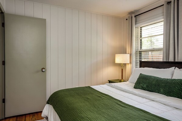 Una habitación de hotel con una cama, una mesita de noche, una lámpara y una ventana con cortinas.