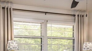 Ein Schlafzimmer mit einem Bett, zwei Nachttischlampen, einem Nachttisch, einem Teppich und einem Fenster mit Jalousien.