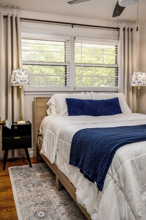A bedroom with a bed, two bedside lamps, a nightstand, a rug, and a window with blinds. - Newly renovated 3/2 in the middle of town (Jonesboro)
