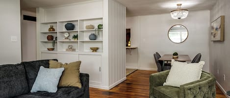 Un saló amb un sofà gris fosc, una butaca verda i un moble d'estanteries blanc amb objectes decoratius.