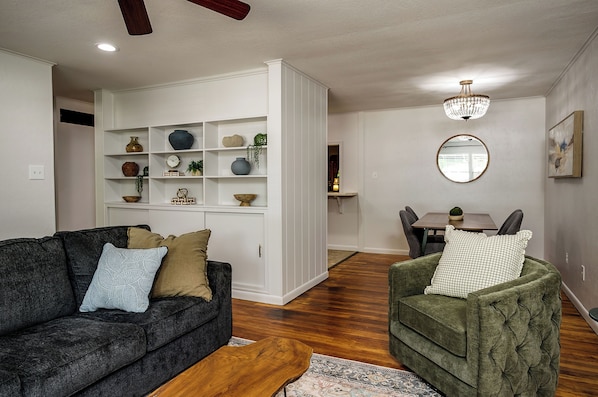 A living room with a dark grey sofa, a green armchair, and a white shelving unit with decorative items.