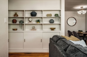A living room with a sofa, a dining table, and a wall-mounted shelf with decorative items.