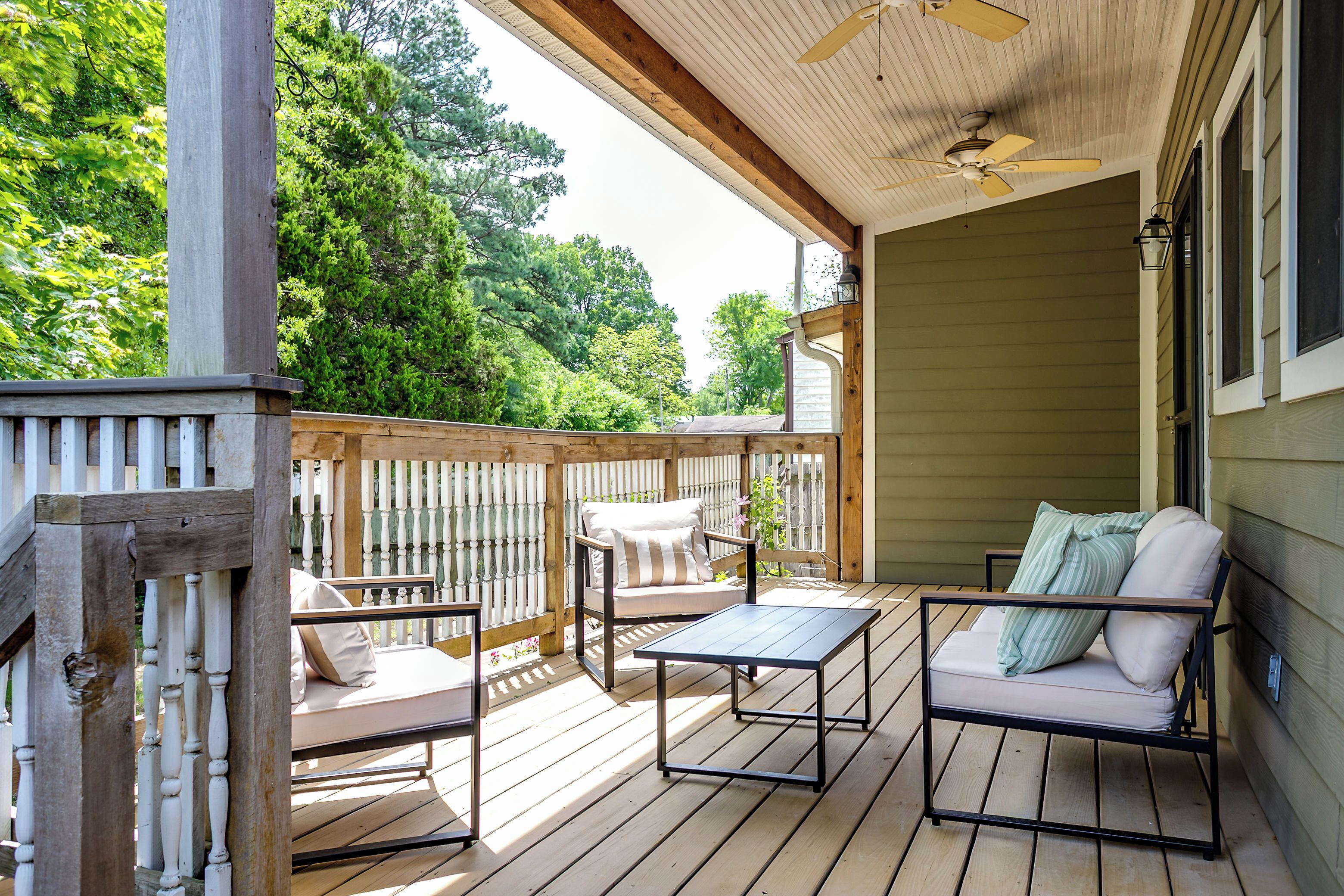 A wooden deck with outdoor furniture, including a sofa and chairs, and a ceiling fan.