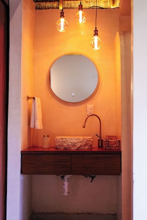 Un baño con un espejo redondo, un tocador de madera, un perchero y un lavabo.