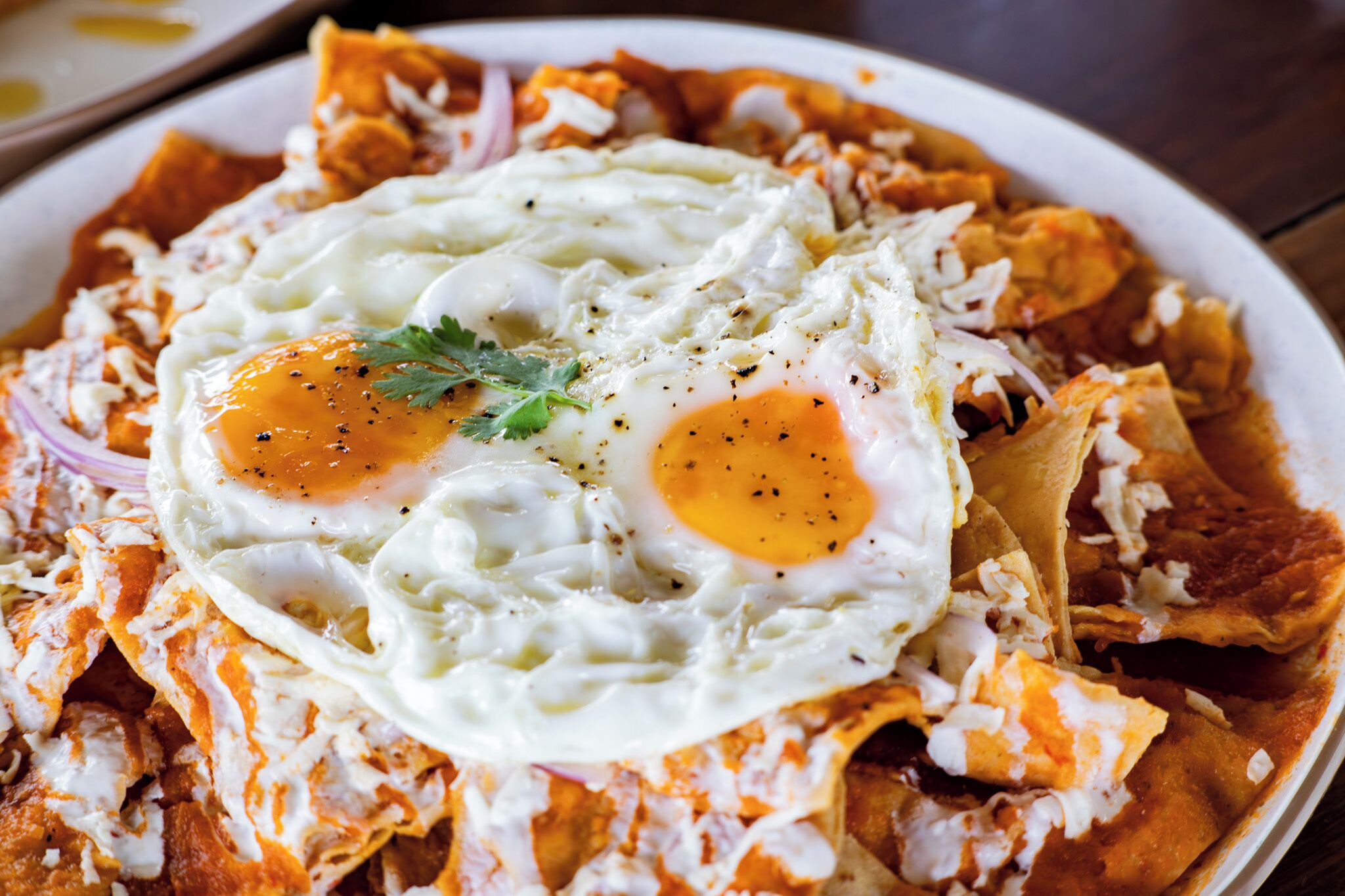 Een bord nachos met twee gebakken eieren en garnering.