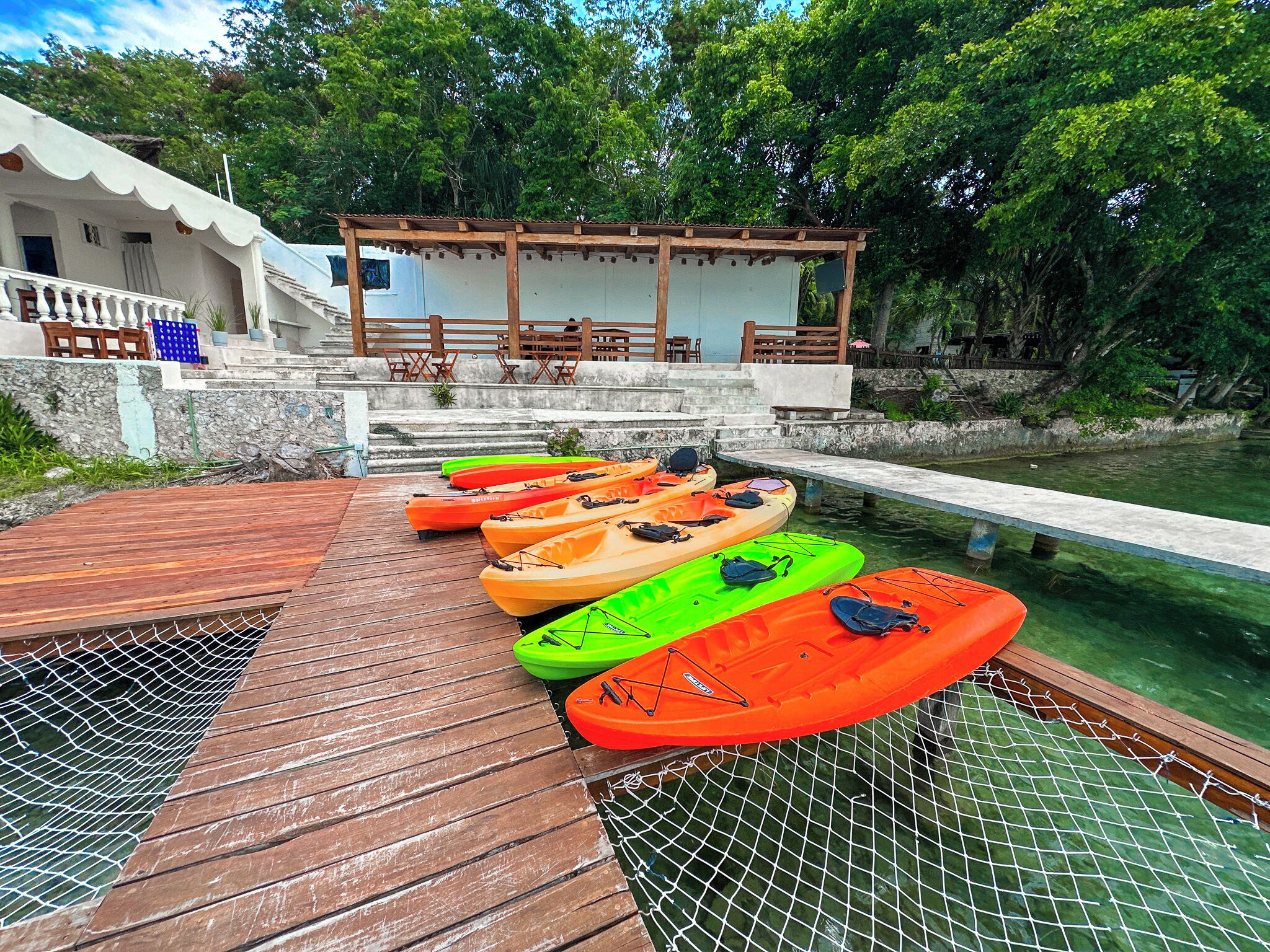 A wooden dock with kayaks lined up, a covered seating area, and a stone wall.