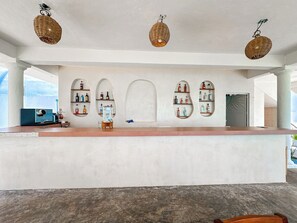 A reception area with a white counter, shelves with bottles, and wicker pendant lights. - GlampCalar (Bacalar)