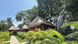 A pathway leading to thatched-roof cottages surrounded by lush greenery. - GlampCalar (Bacalar)