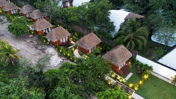 A resort with thatched-roof cottages arranged in a row, surrounded by lush greenery and palm trees.