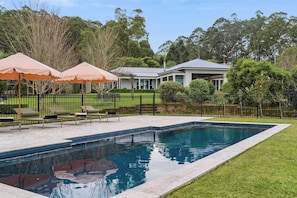 Ein Schwimmbecken mit gepflastertem Sonnendeck, Liegestühlen und Sonnenschirmen.