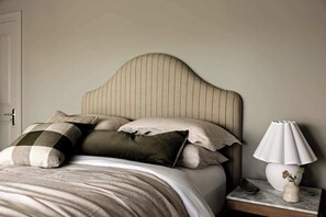Ein Bett mit Kopfteil, Kissen, einem Nachttisch mit Lampe und einer Vase mit Blumen.