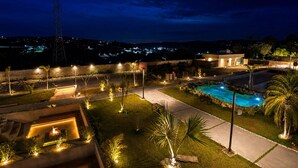Nattebillede af et resort med swimmingpool, godt oplyste stier og et fjerntliggende elmastværk.