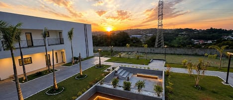 A modern building with a fire pit and outdoor seating area, surrounded by palm trees and a sunset view.