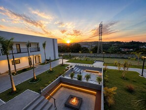 Ein modernes Gebäude mit Feuerstelle und Sitzbereich im Freien, umgeben von Palmen und Blick auf einen Sonnenuntergang.