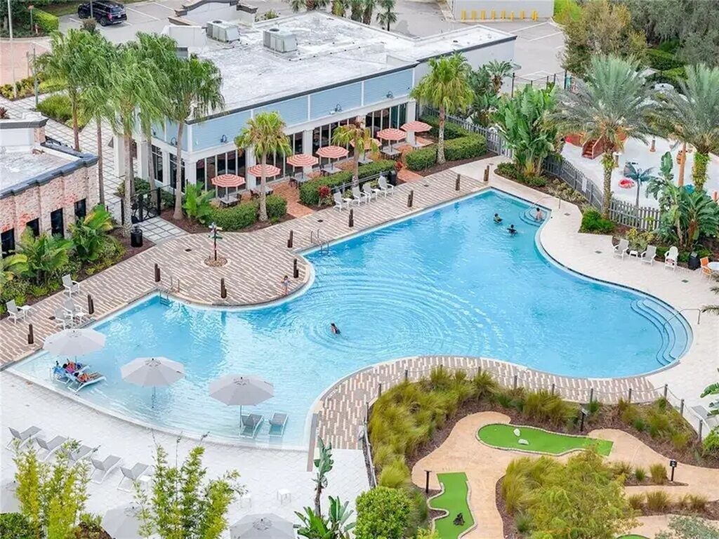 A swimming pool with a curved edge, surrounded by lounge chairs and umbrellas, and adjacent to a building with a flat roof.
