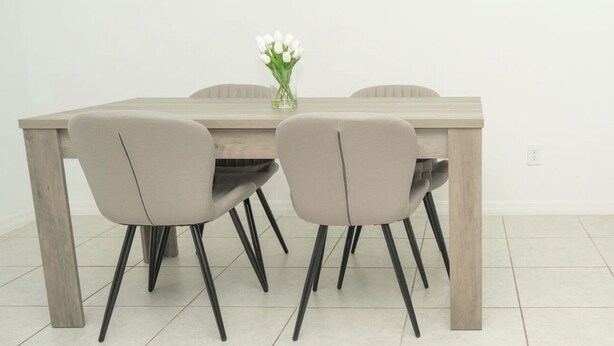 Una mesa de comedor con cuatro sillas, un jarrón con flores y dos marcos de fotos vacíos en la pared.
