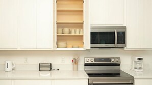 Una cocina con armarios blancos, microondas, horno, tostadora y cafetera.