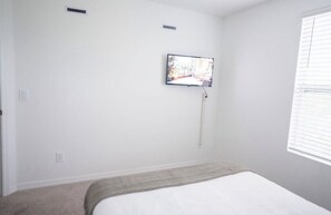 Una camera da letto con un letto, una televisione a muro e una finestra con persiane.
