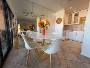 A modern dining area with a round table, white chairs, and a vase of sunflowers. - Big Beautiful Bed, View and Balcony! (Palm Springs)