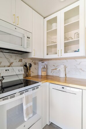 A kitchen with white cabinets, a microwave, an oven, and a dishwasher. - Big Beautiful Bed, View and Balcony! (Palm Springs)