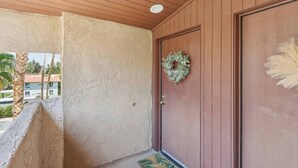 A wooden door with a wreath, a textured wall, and a palm tree outside. - Big Beautiful Bed, View and Balcony! (Palm Springs)