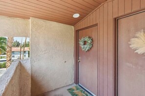 A wooden door with a wreath, a textured wall, and a palm tree outside. - Big Beautiful Bed, View and Balcony! (Palm Springs)