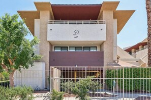 A modern building with a flat roof, a balcony on the upper level, and a gated entrance. - Big Beautiful Bed, View and Balcony! (Palm Springs)