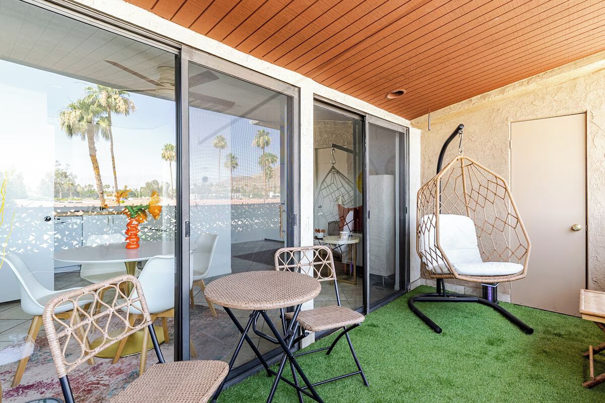 Un espace de détente extérieur moderne, doté d’un mur de verre, d’un fauteuil suspendu et d’une petite table avec des chaises.