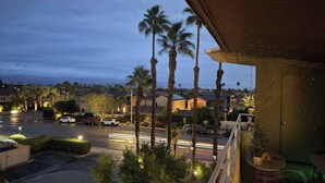 A residential area at dusk with palm trees, a street with cars, and a building with a balcony. - Big Beautiful Bed, View and Balcony! (Palm Springs)