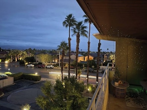 A residential area at dusk with palm trees, a street with cars, and a building with a balcony. - Big Beautiful Bed, View and Balcony! (Palm Springs)
