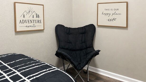 A bedroom with a bed, a black chair, and two framed motivational posters on the wall.