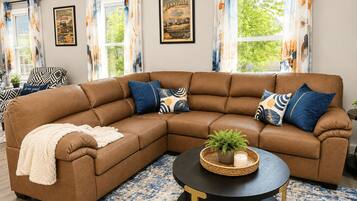 A living room with a brown sectional sofa, patterned cushions, a black coffee table with a plant, and a blue patterned rug.