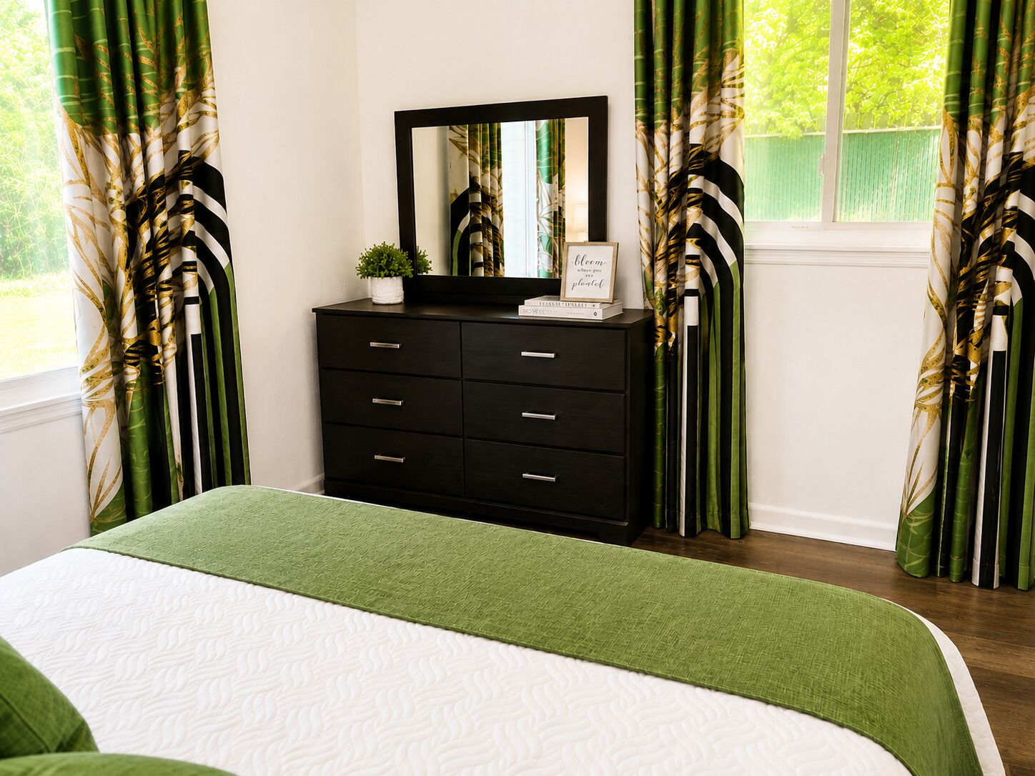 A bedroom with a bed, a dresser, a mirror, and curtains with a leaf pattern.