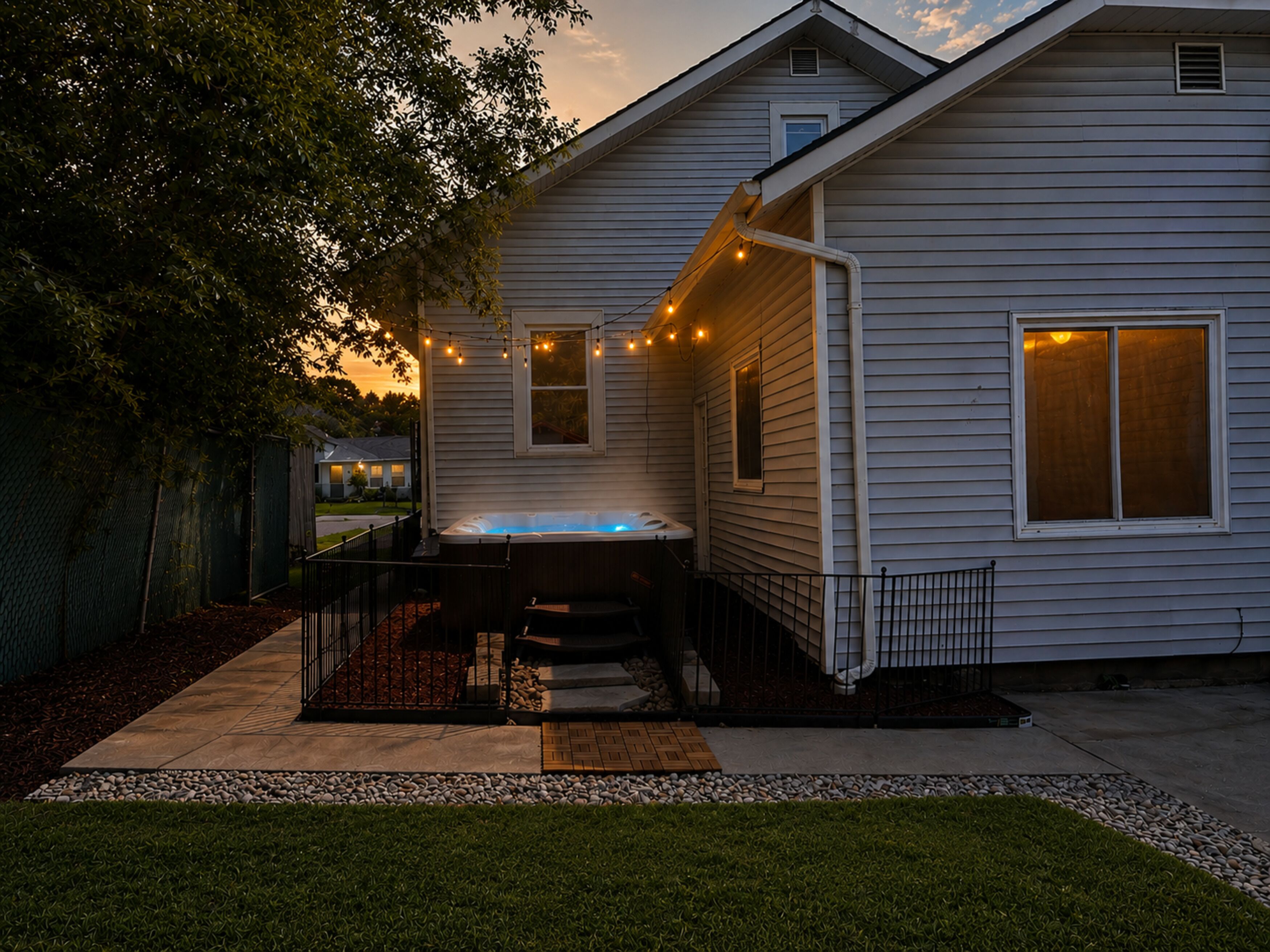 A residential house with a visible outdoor hot tub, a fenced yard, and a clear sky.