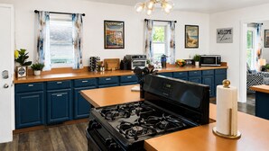 A modern kitchen with a gas stove, a microwave, and a coffee machine. There are two windows with curtains, and a ceiling light fixture.