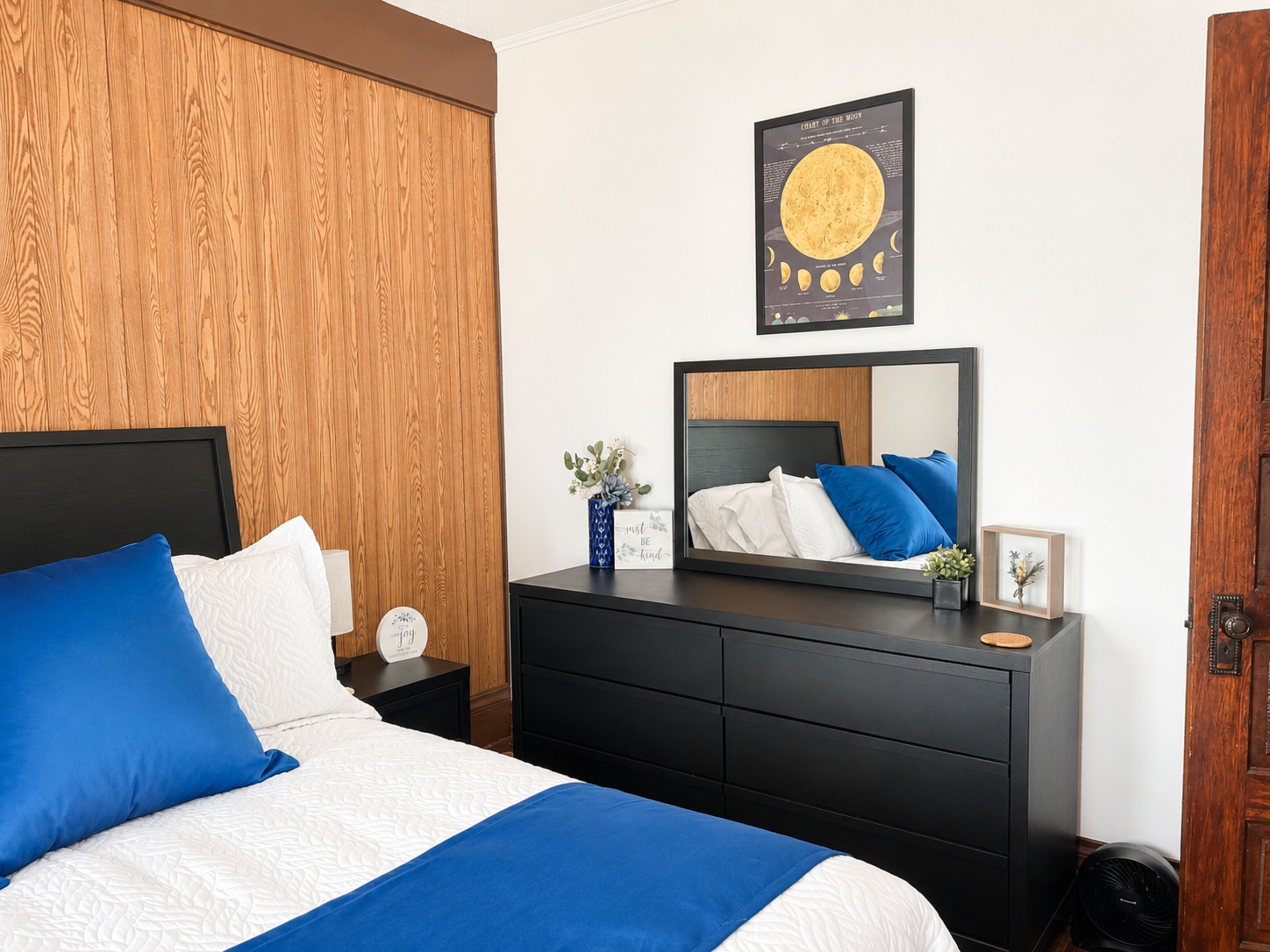 Un dormitorio con cama, cómoda, espejo y un gráfico de la luna colgado en la pared.