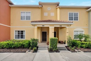 A two-story building with a yellow facade, a tiled roof, and a front entrance with a door and windows. - Paradise Palms Family Oasis (Kissimmee)